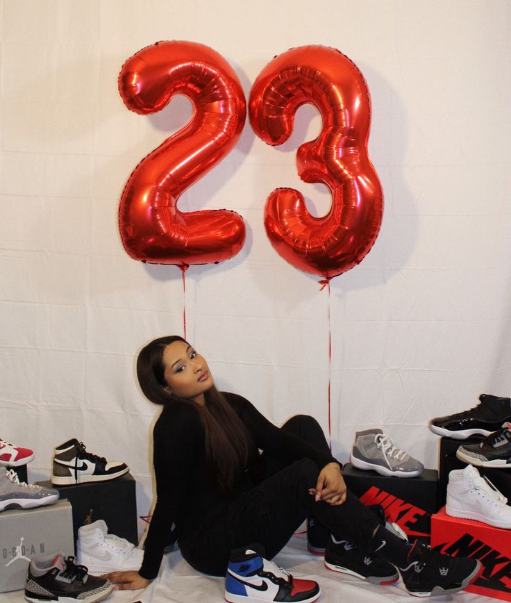 a woman sitting on the floor with red balloons in front of her and shoes all around her