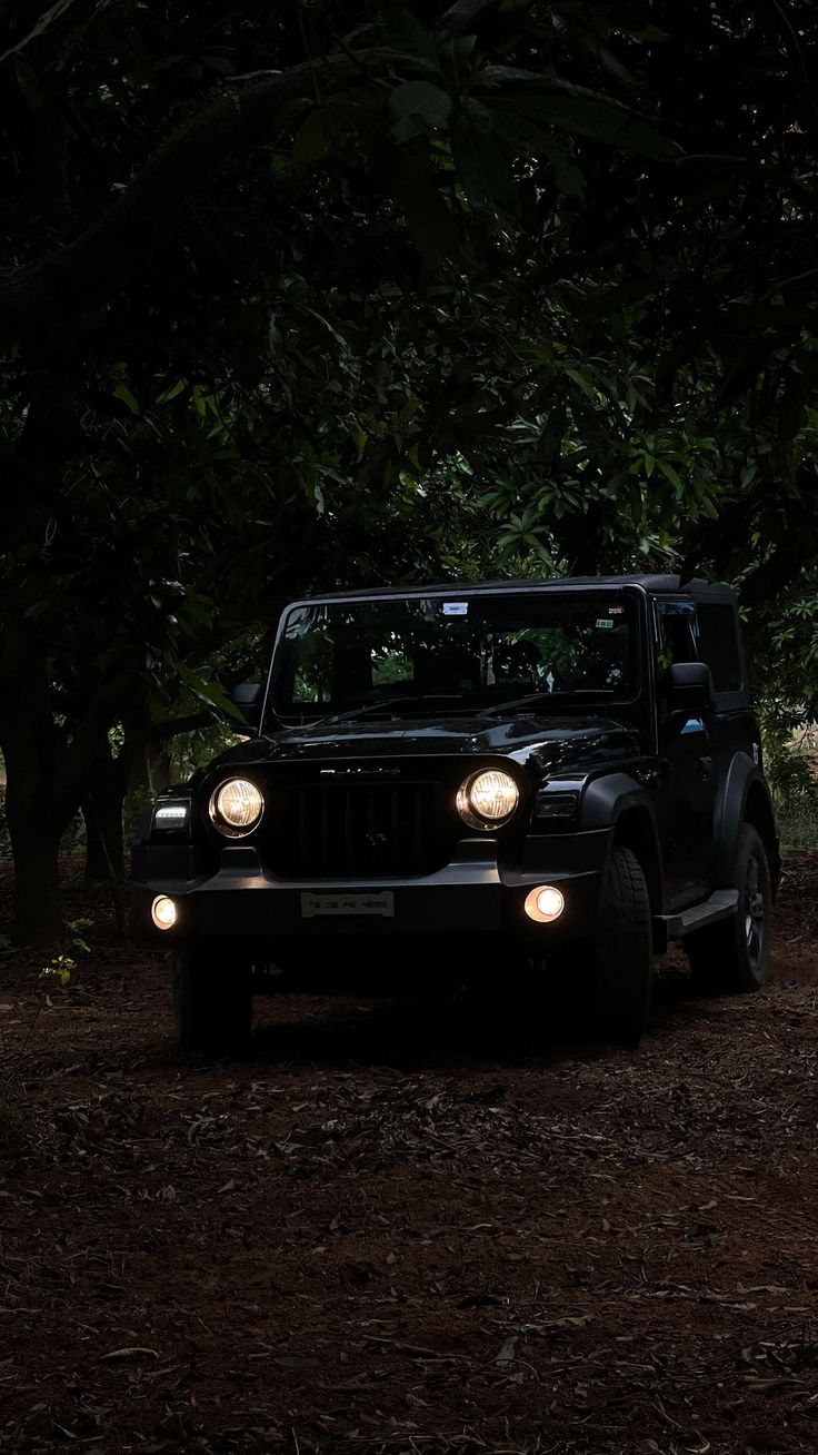 a jeep is parked in the woods at night with its headlights turned on and it's headlamps glowing