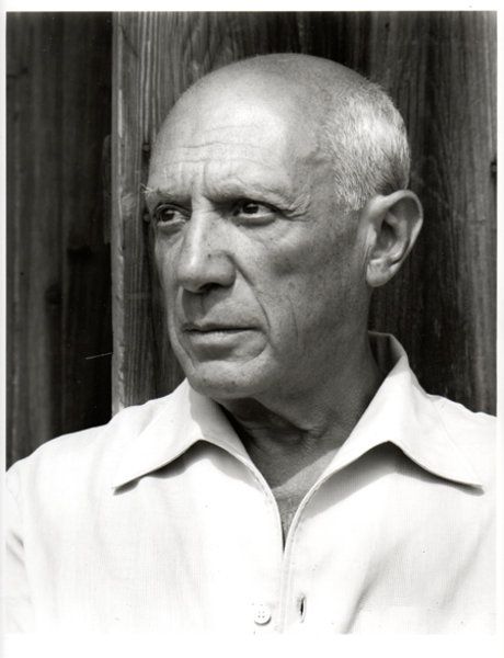 black and white photograph of an older man in front of a wooden fence looking at the camera