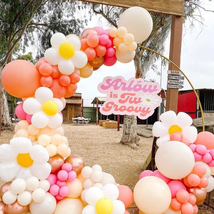 a bunch of balloons that are in the dirt near a sign and some trees with flowers on it