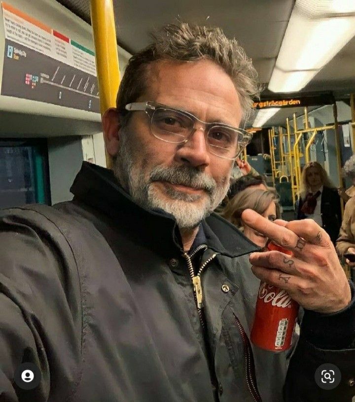 a man wearing glasses and a black jacket on a train holding onto a red cup