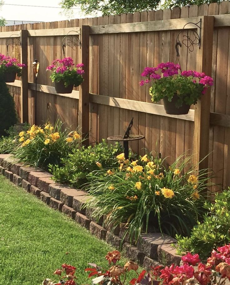 a garden with flowers and plants growing on the fence