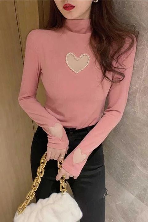 a woman wearing a pink sweater and black pants holding a white purse with a heart on it