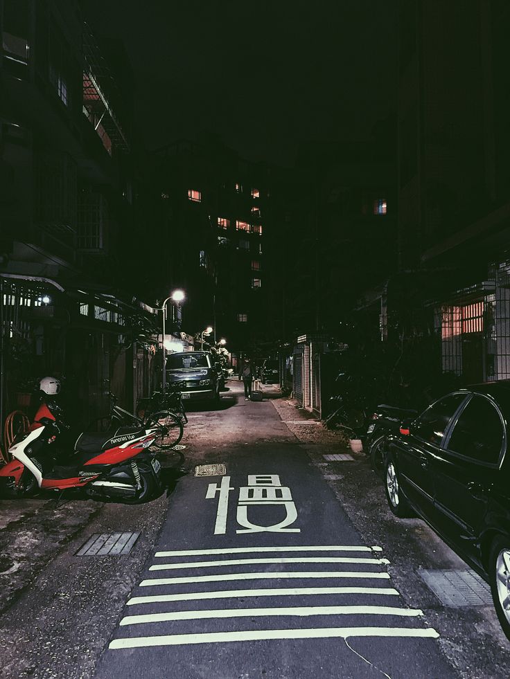 an empty street at night with cars and motorcycles parked on the side walk next to it