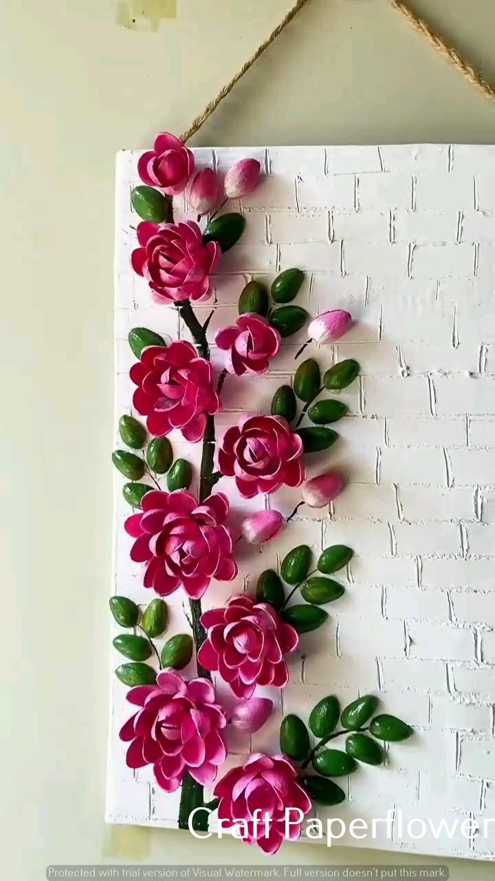 pink paper flowers are hanging on a white brick wall with green leaves and twine