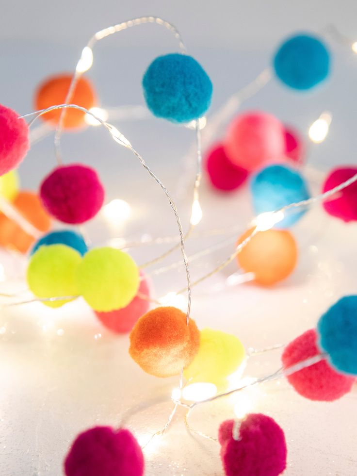 multicolored pom - poms are strung with string lights on a white surface