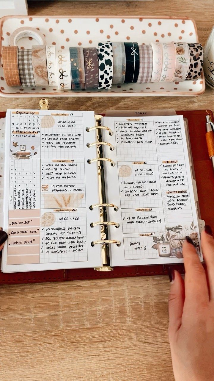 a person holding a pen and looking at an open planner on a desk with washi tapes