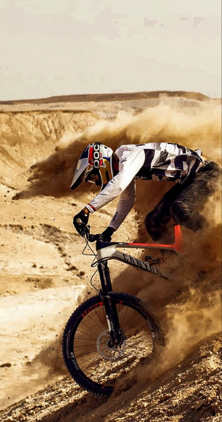 a man riding a bike on top of a dirt covered slope in the desert with dust blowing up around him