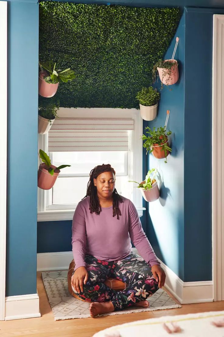 a woman sitting on the floor in front of a window with potted plants hanging from it