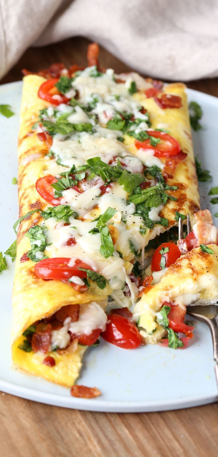 an omelet with tomatoes, cheese and parsley on a plate next to a fork