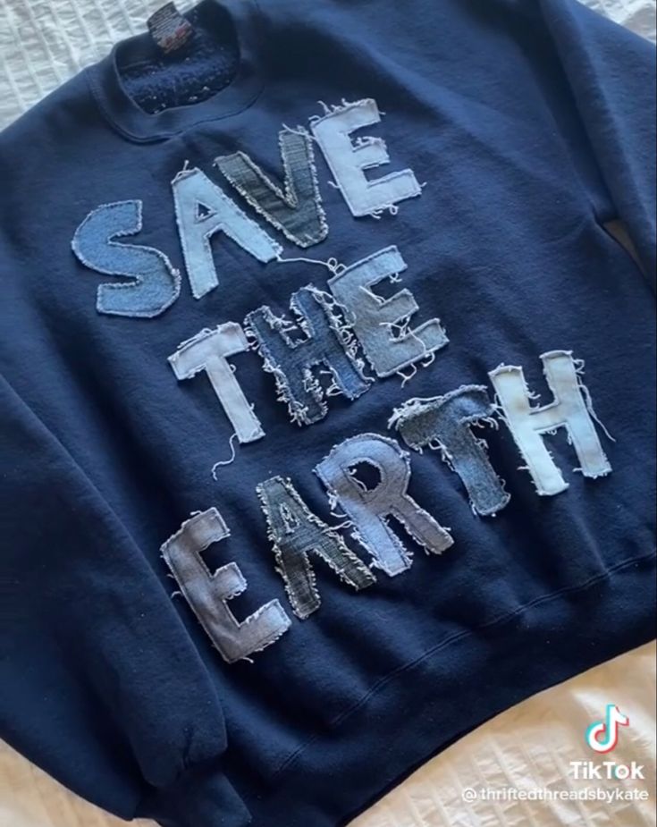 a blue sweatshirt with the words save the earth printed on it sitting on a bed