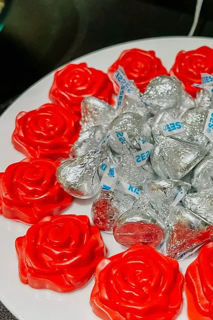 there is a white plate with red roses on it and candy in the shape of hearts