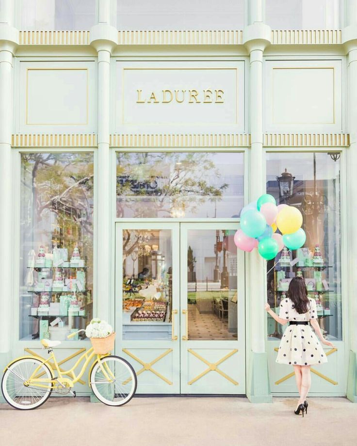 a woman is holding balloons in front of a storefront with a bicycle parked outside