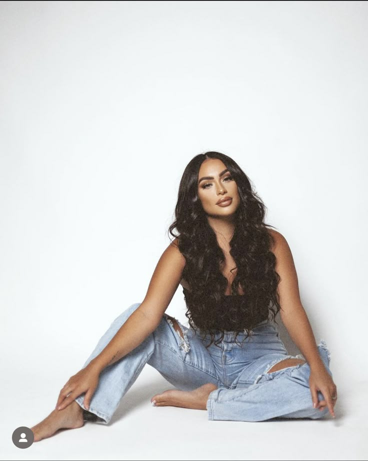 a woman is sitting on the floor with her legs crossed and wearing ripped denims