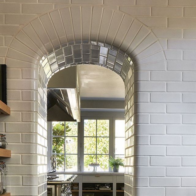 an arched window in a white brick wall with wooden shelves on either side and a kitchen counter below