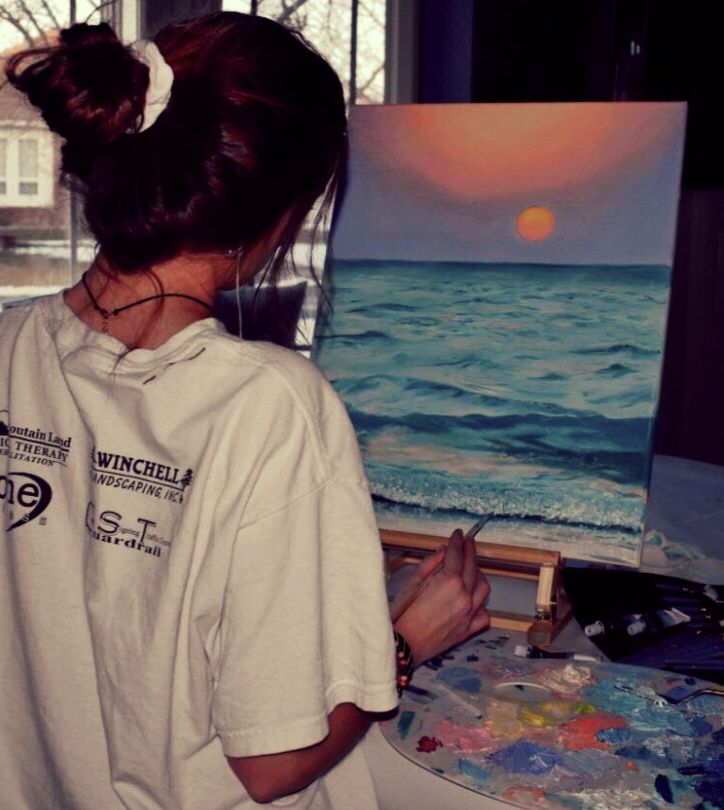 a woman standing in front of an easel holding a paintbrush and looking at the ocean