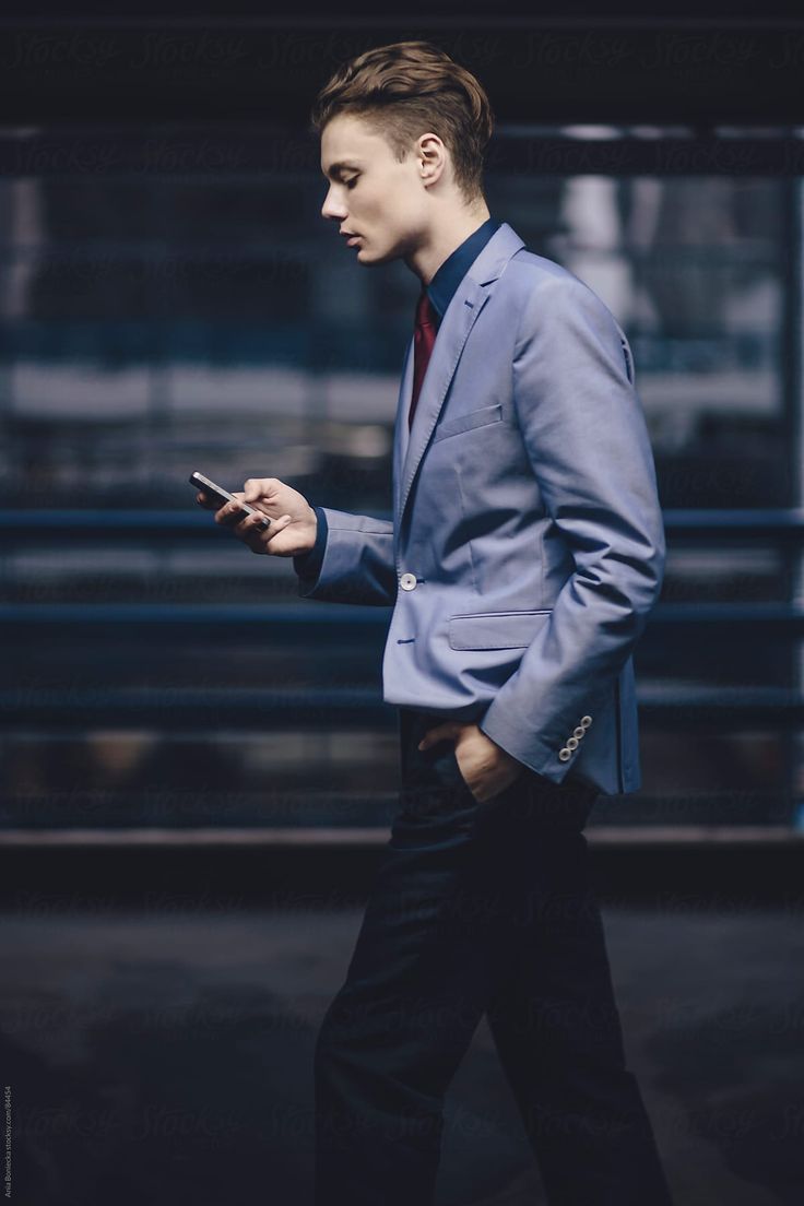 a man in a blue suit and red tie is looking at his cell phone while walking down the street