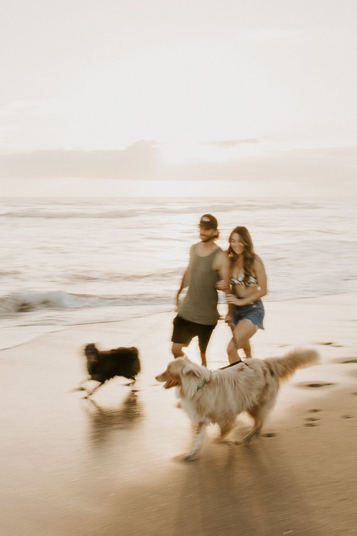 two people and a dog running on the beach