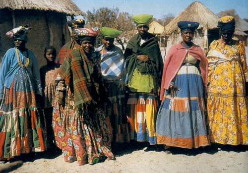 a group of people standing next to each other in front of some thatched huts