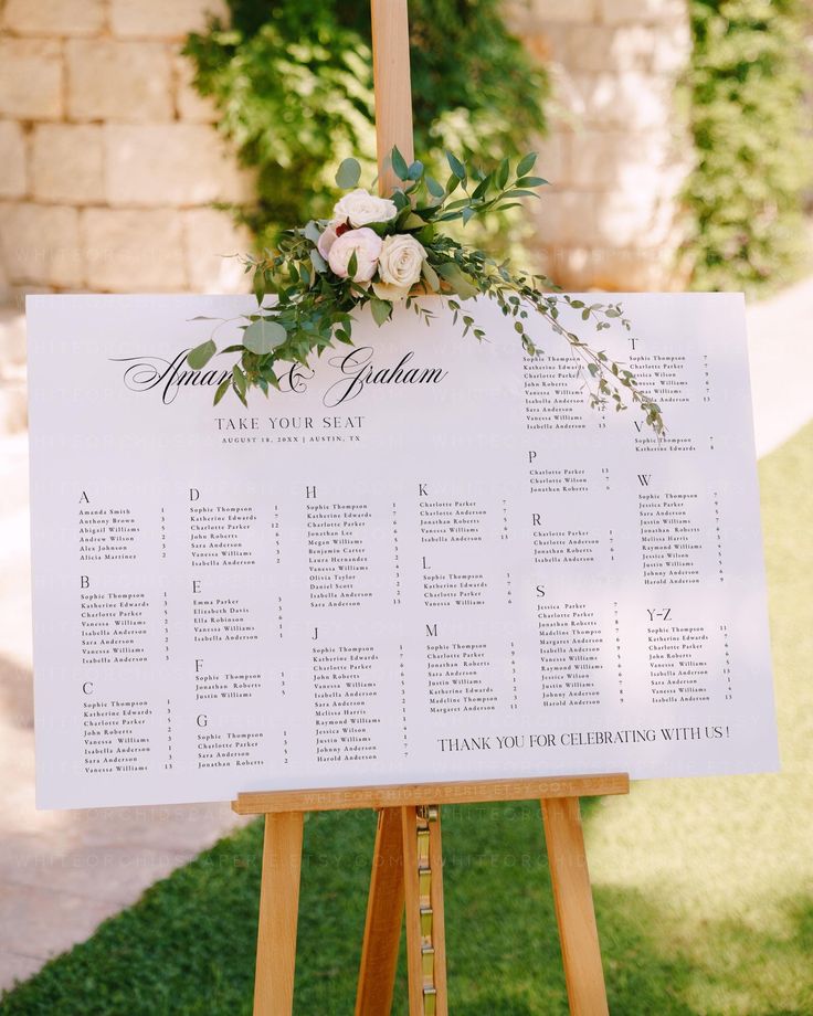 a wooden easer with a seating chart and flowers on it for an outdoor wedding