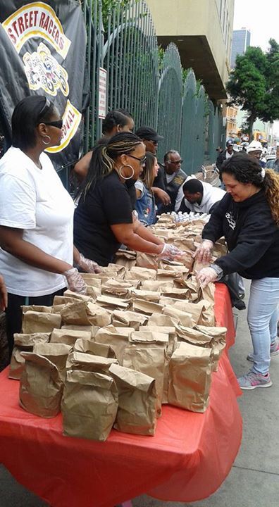 several people standing around a table with bags on it and one person handing out some food