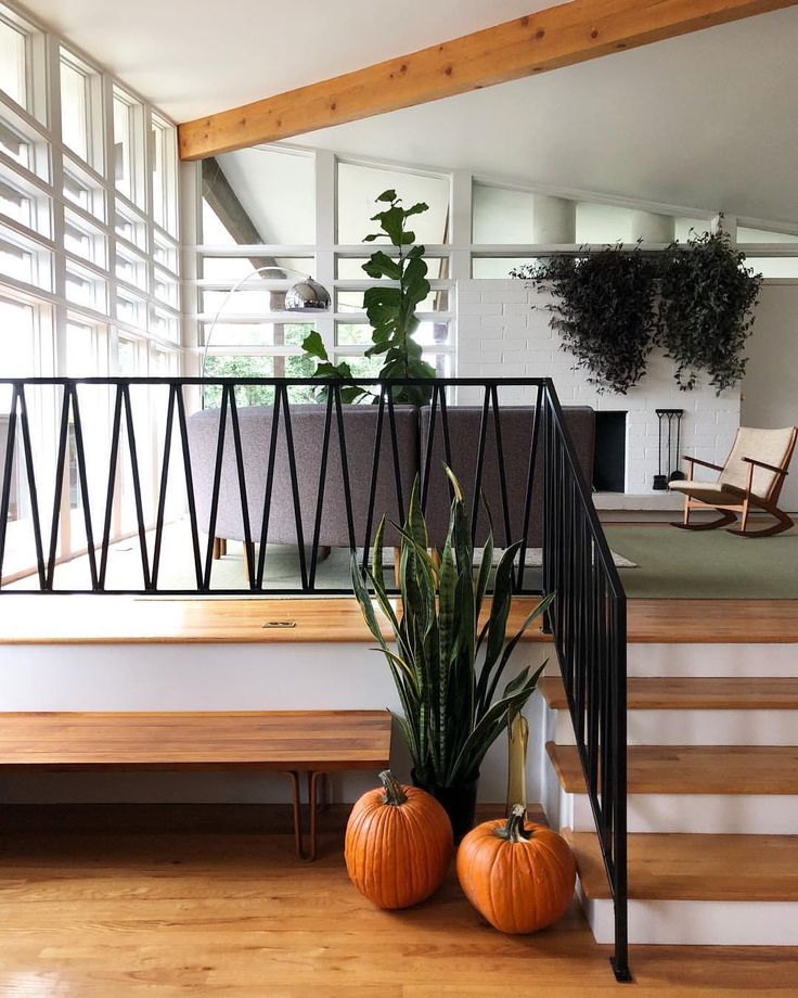 two pumpkins are sitting on the floor next to a stair case and potted plant