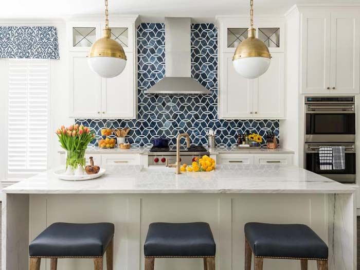 a kitchen with white cabinets and blue patterned backsplash, gold pendant lights over the island