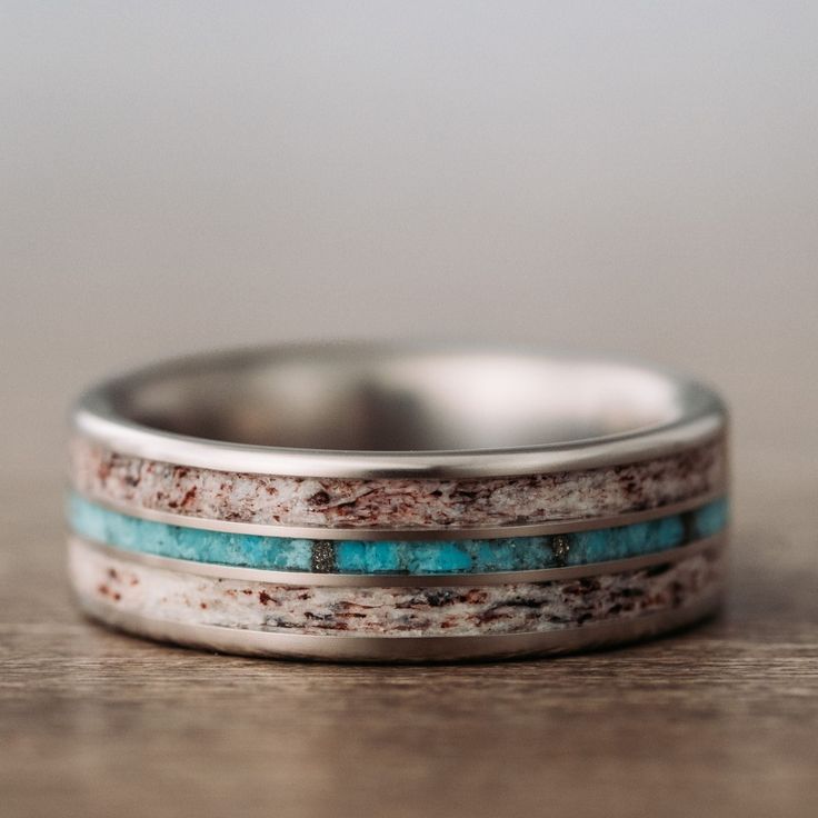 a wedding band with turquoise and white inlays sits on top of a wooden table