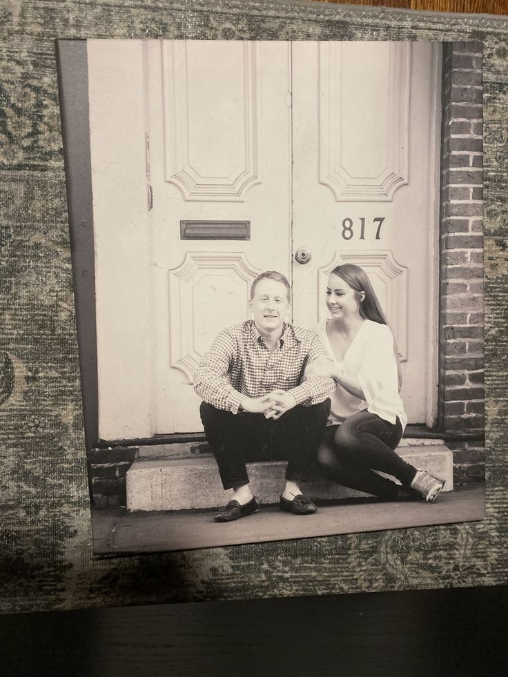 an old black and white photo of two people sitting on the steps in front of a door