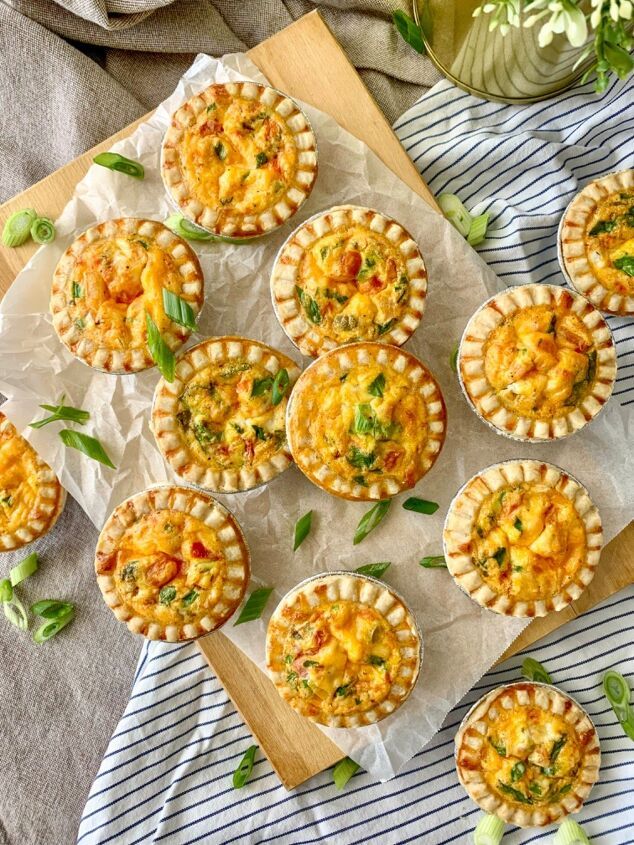 mini quiche pies with cheese and vegetables on a cutting board next to flowers