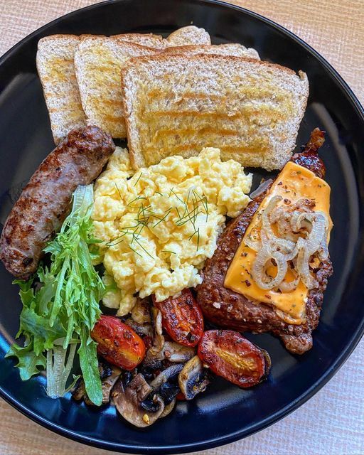 a black plate topped with meat, eggs and toast