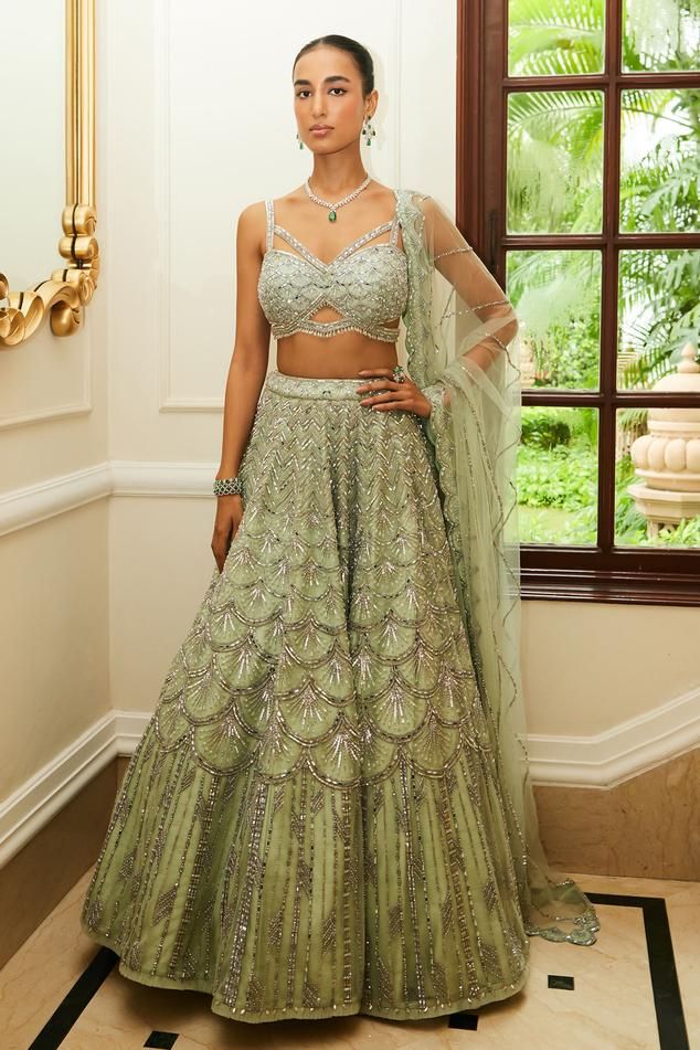 Mint green attached cancan flared lehenga with all-over scallop spark tonal embroidery highlighted with sequin, silver beads and crystals. Paired with sweetheart neck cut out detail embellished sleeveless padded blouse and scallop embroidered net dupatta.
Components: 3
Pattern: Embroidery
Type Of Work: Tonal Silver Beads, Sequins, Crystals
Neckline: Sweetheart Neck
Sleeve Type: Strap Sleeves
Fabric: Net, Raw Silk
Color: Green
Other Details: 
Attached cancan
Padded blouse
Blouse with bead drops
A Wedding Saree Gown In Green, Green Lehenga For Reception, Anarkali Style Embellished Green Choli, Elegant Pista Green Choli For Reception, Embellished Green Floor-length Traditional Wear, Green Anarkali Style Embellished Lehenga, Elegant Pista Green Choli With Intricate Embroidery, Anarkali Embellished Green Choli, Green Bollywood Style Embellished Lehenga