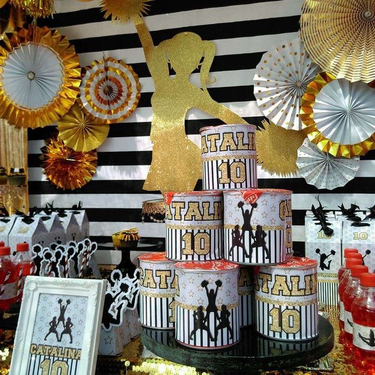 a table topped with lots of cake covered in gold and black paper decorations next to framed pictures