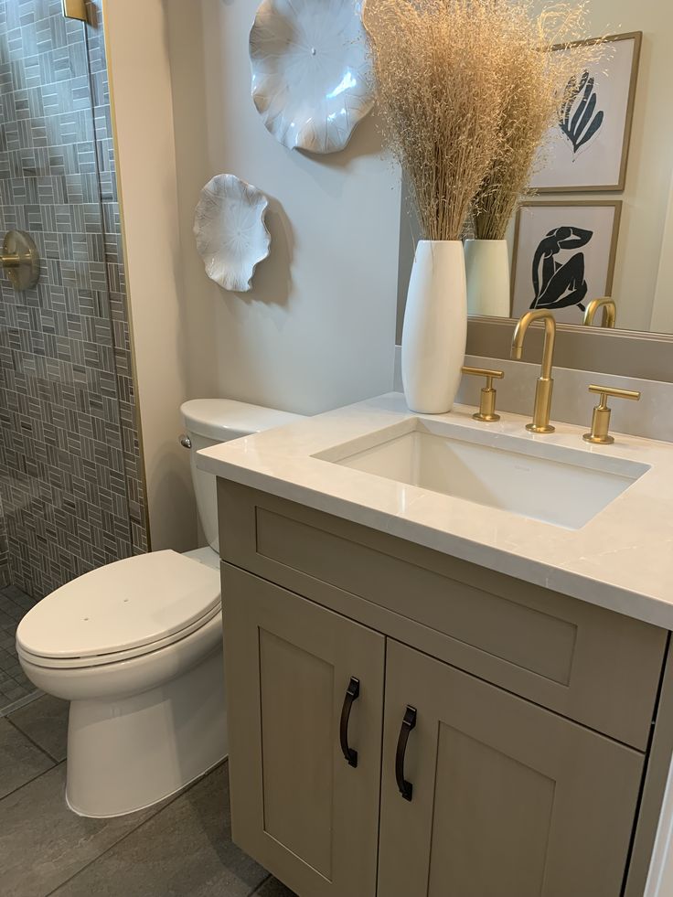 a white toilet sitting next to a sink in a bathroom under a mirror and a vase with dry grass