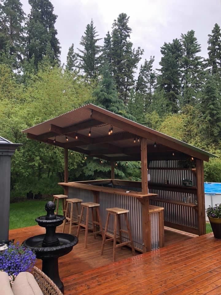 an outdoor bar with stools and tables on a deck in front of some trees