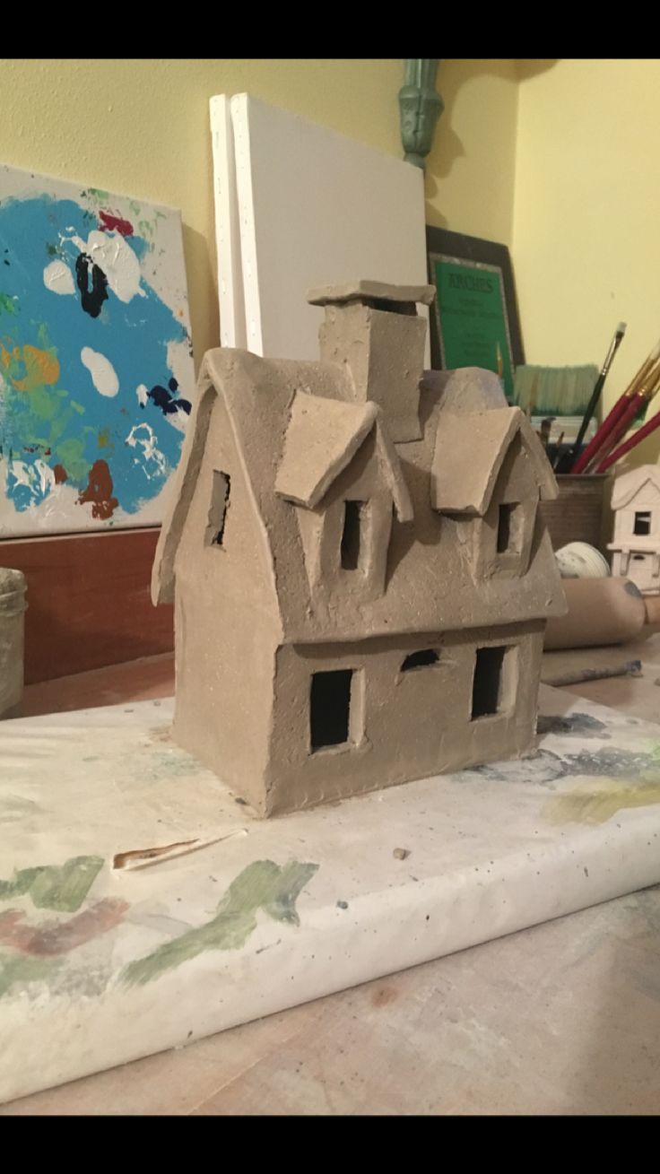 a clay house sitting on top of a table next to paintbrushes and paper