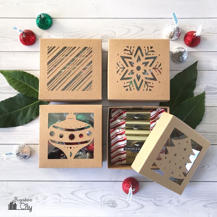 four boxes with christmas ornaments and decorations in them on a white wooden table next to green leaves