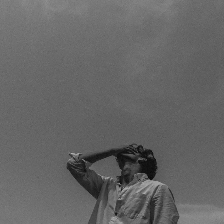 black and white photograph of a man holding a baseball bat over his head with clouds in the background