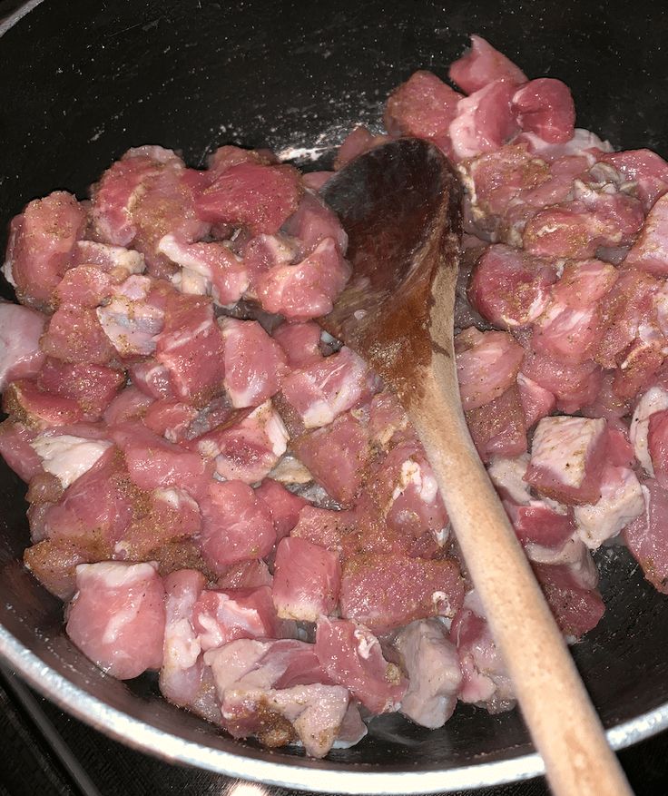 meat cooking in a pan with a wooden spoon