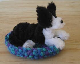 a small black and white dog sitting in a blue crocheted basket on a wooden table