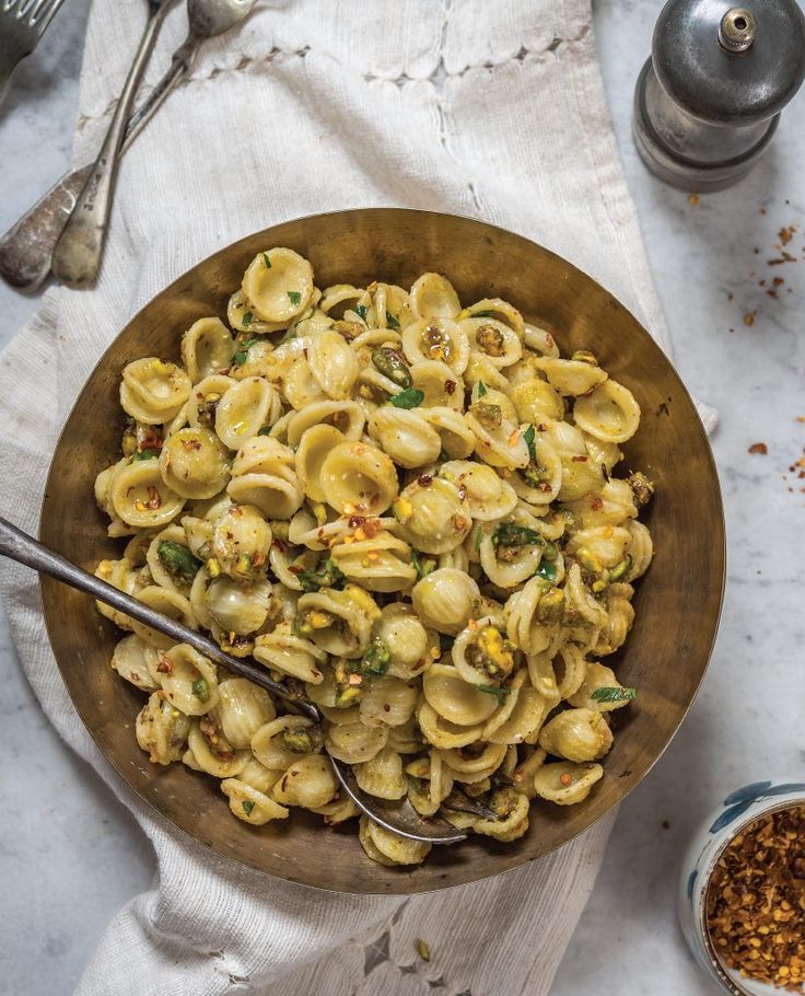 a wooden bowl filled with pasta on top of a white cloth next to silverware