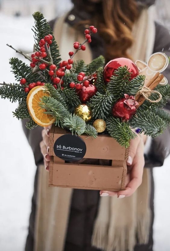 a woman is holding a box filled with christmas decorations