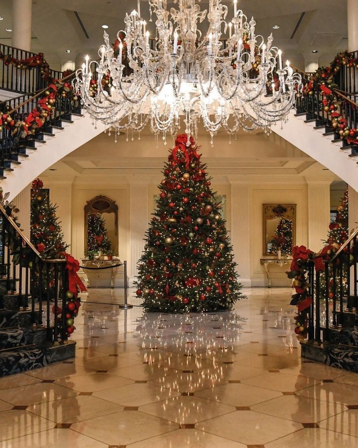 a christmas tree in the middle of a lobby with chandelier and staircases