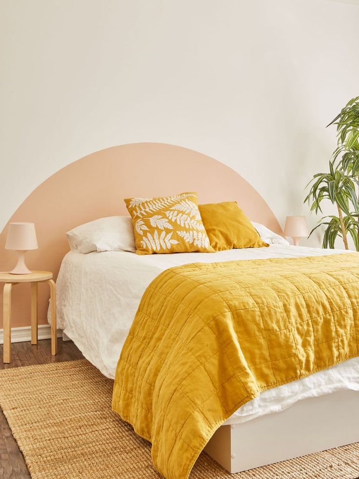 a bed with yellow blankets and pillows in a bedroom next to a potted plant