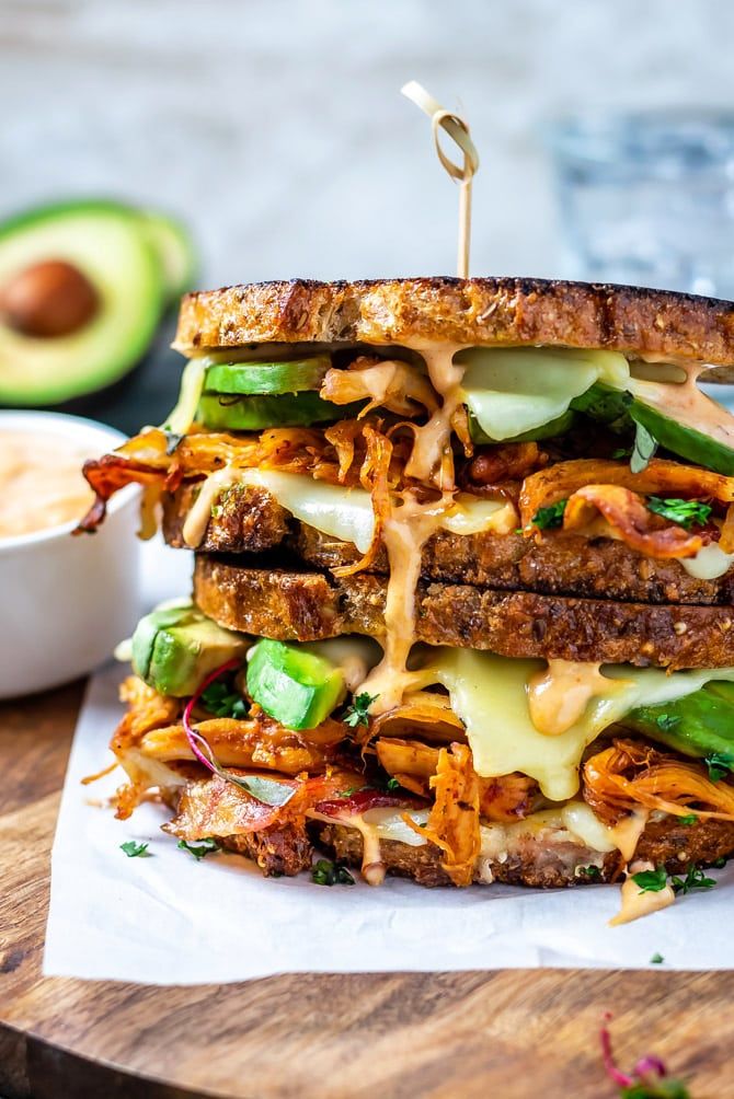 a grilled sandwich with cheese, lettuce and other toppings on a cutting board