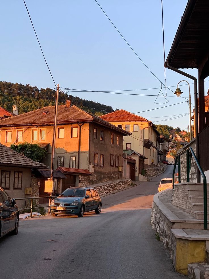 cars are parked on the street in front of some houses and buildings with mountains in the background