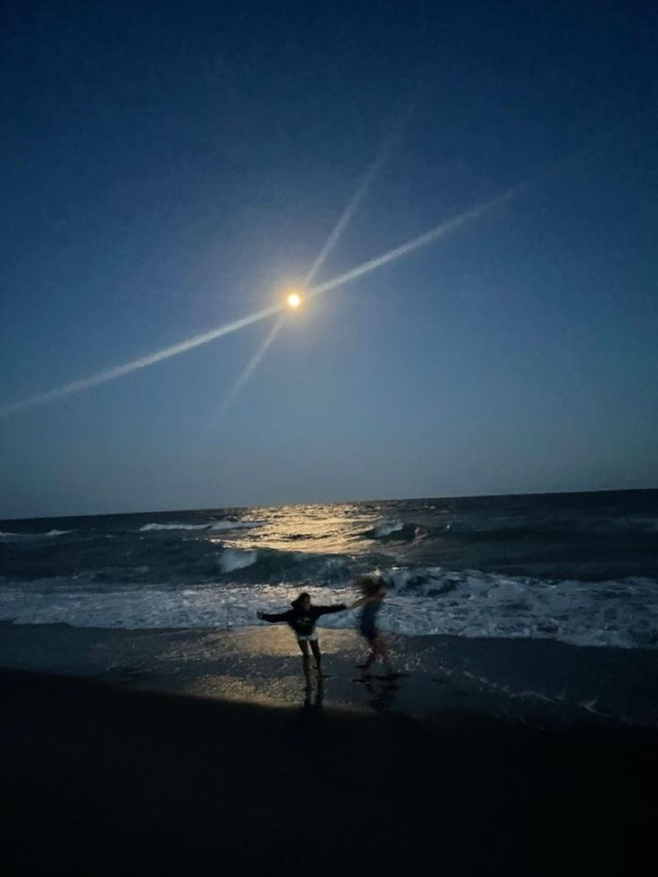 two people are standing on the beach at night with their arms spread out in front of them