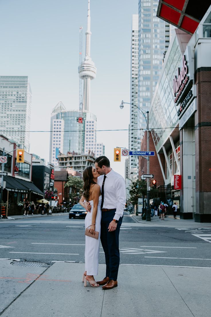 a man and woman standing on the sidewalk in front of a city street with tall buildings