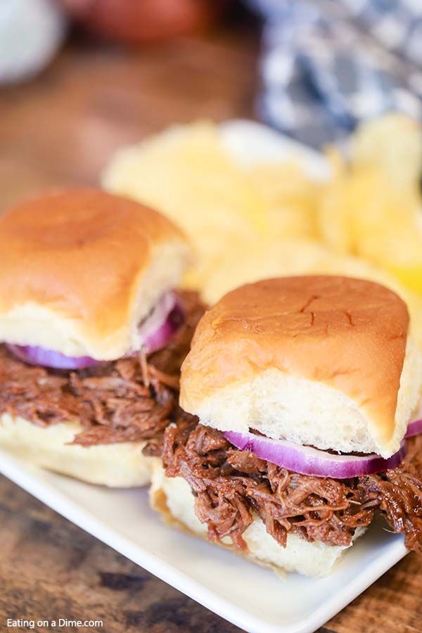 two pulled pork sandwiches with red onions on a white plate next to some potato wedges