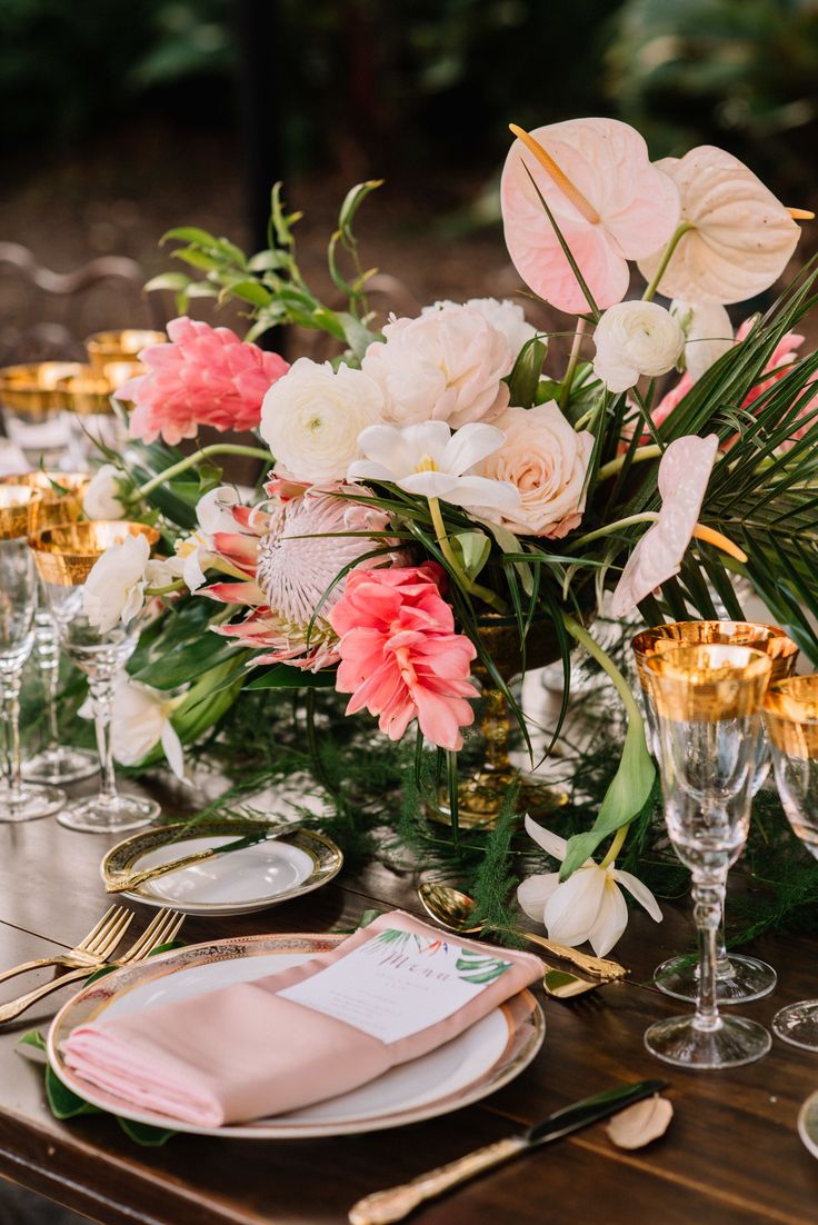 the table is set with pink and white flowers, gold place settings, and greenery